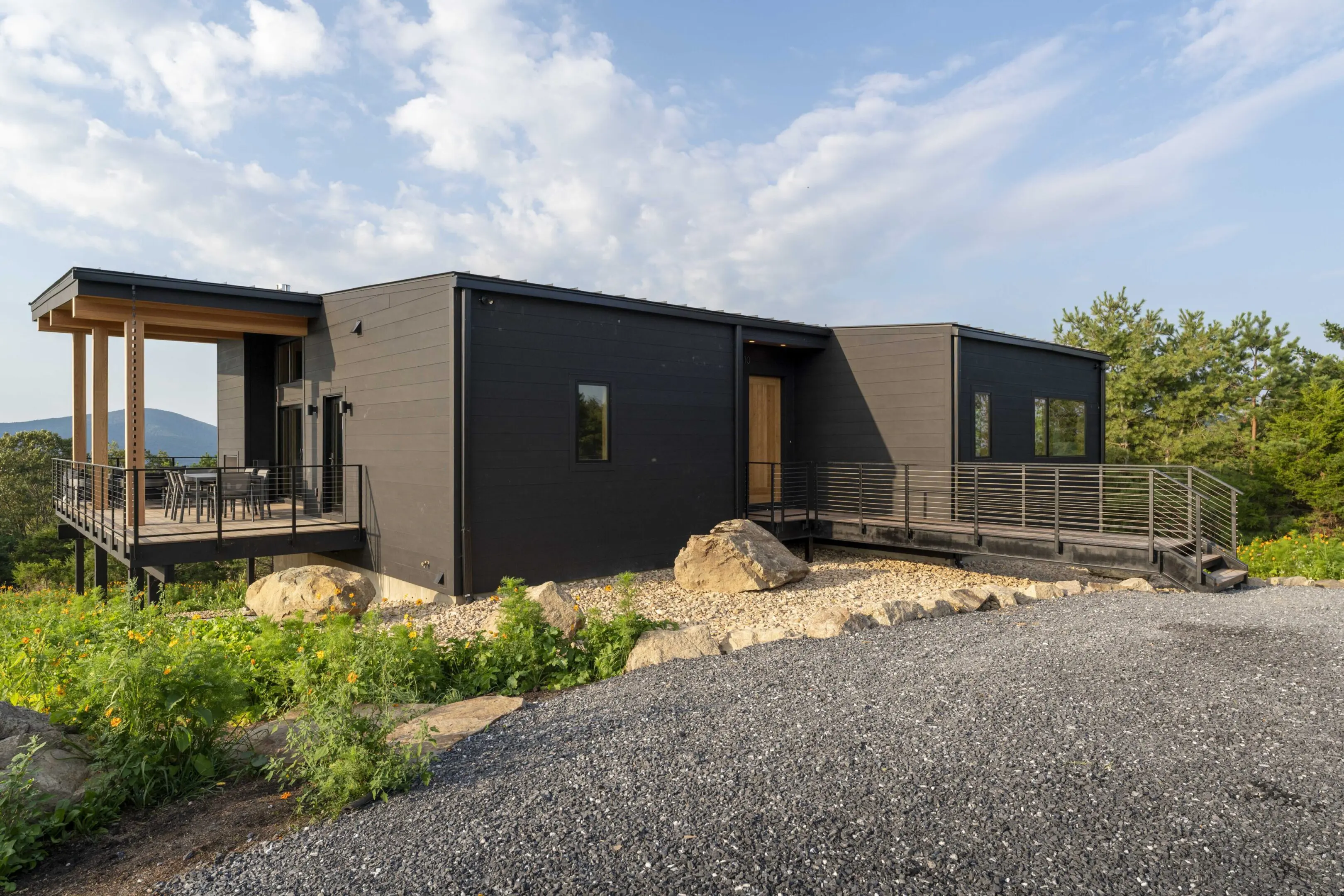 A black container house with a porch and a gravel driveway.