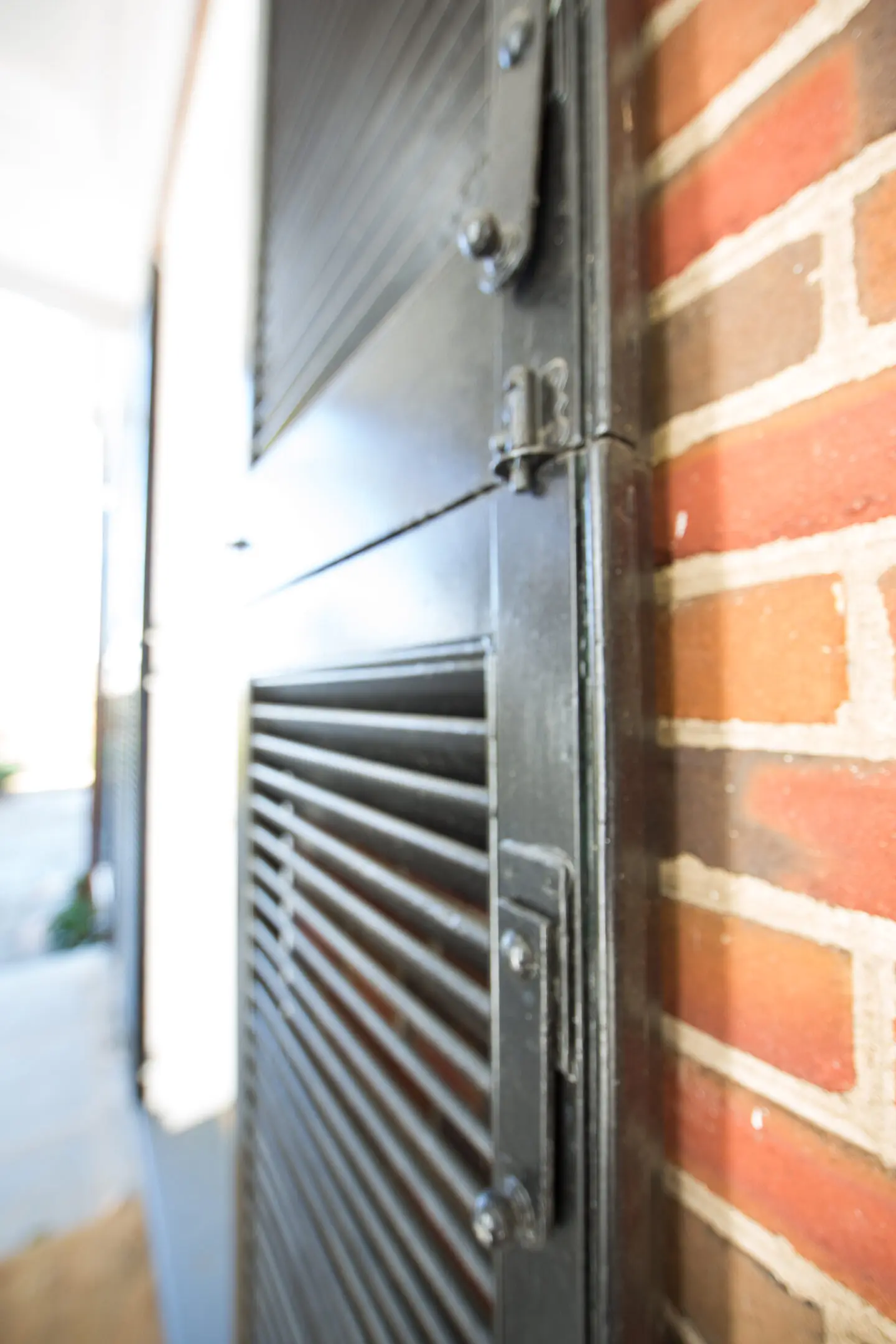 A black metal door with a brick wall in the background.