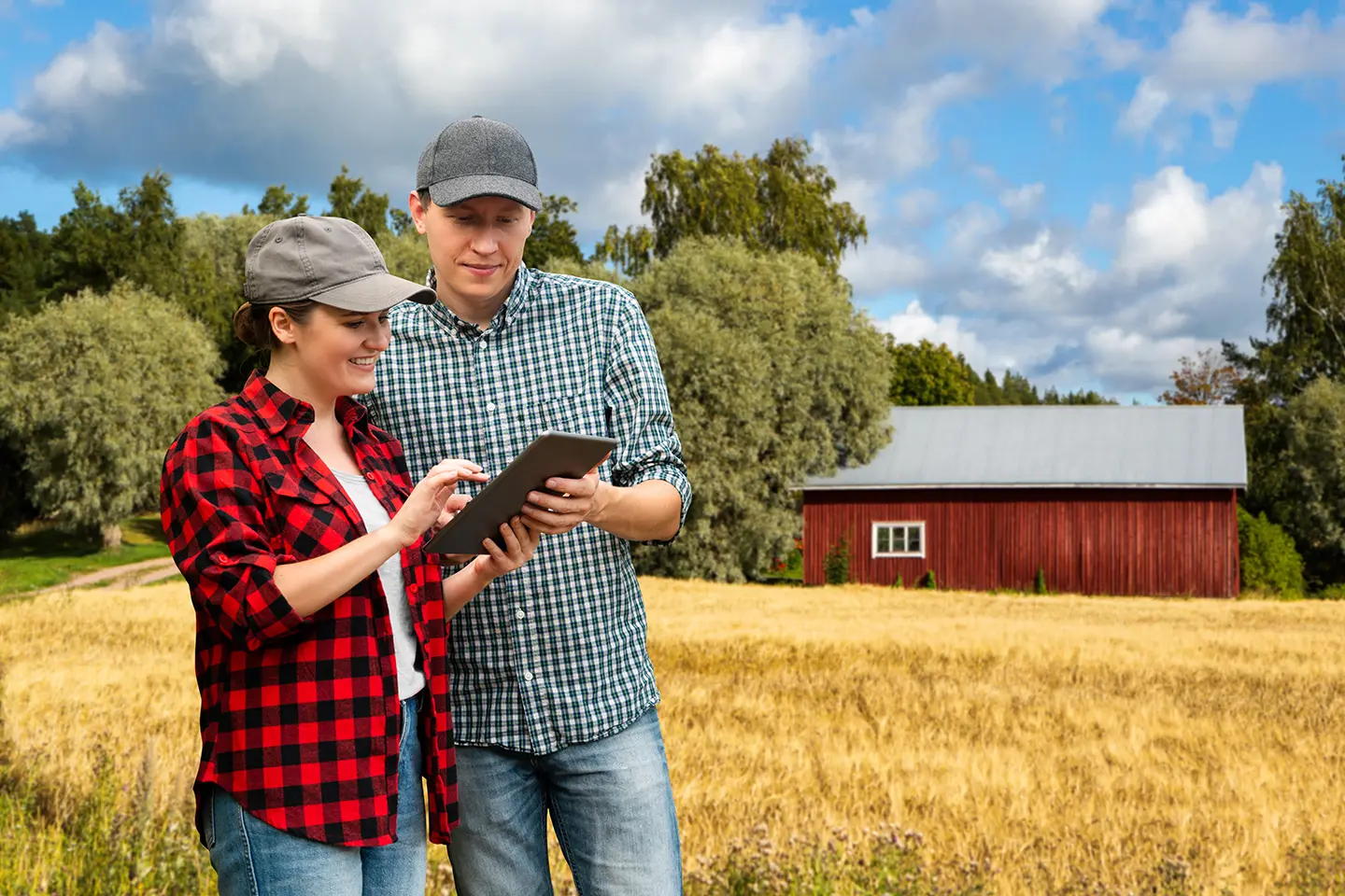 A man and woman looking at an ipad in front of a barn.